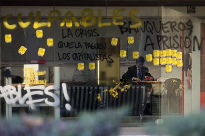 Un trabajador, en el interior de una entidad bancaria con las ventanas cubiertas de pegatinas y pintadas.