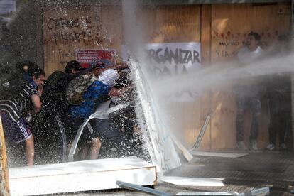 Un grupo de manifestantes se protege en las calles de Santiago de Chile frente al cañón de agua utilizado por las fuerzas de seguridad para reprimir las protestas contra la política económica del Gobierno chileno.