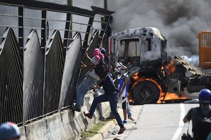 Un grupo de activistas de la oposición venezolana tratan de derriban un valla mientras arde un camión durante las protestas frente a la base aérea.