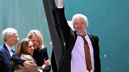 Assange saluda a sus seguidores mientras su esposa y abogada, Stella Assange, de cabello castaño, se abraza con otra letrada de su equipo legal, en el aeropuerto de Canberra, el 26 de junio de 2024.