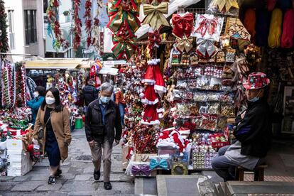 People (L) walk past a stall selling Christmas decorations in Hong Kong on December 2, 2022. (Photo by ISAAC LAWRENCE / AFP)