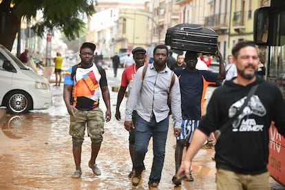 Varias personas caminan por una calle anegada en el barrio de La Torre en Valencia, este miércoles.