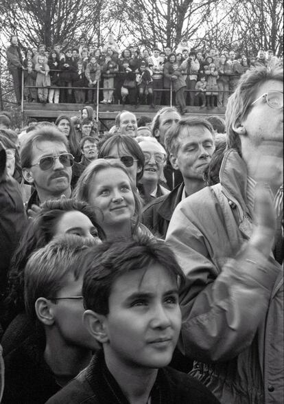 Berlinenses ocidentais observam um soldado, que não aparece na foto, subir no Muro perto do Portão de Brandemburgo, de onde grita e aplaude eufórico pelo fim da Guerra Fria.