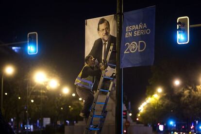 Un operario coloca un cartel del candidato del Partido Popular, Mariano Rajoy, en el Paseo de la Castellana.