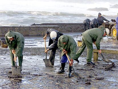 Equipos de limpieza, sin guantes, trabajaban ayer en la playa de Muxia (A Coruña), invadida por el fuel.