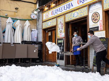 Trabajadores de un bar limpian de nieve la terraza de un local en Madrid, este domingo.