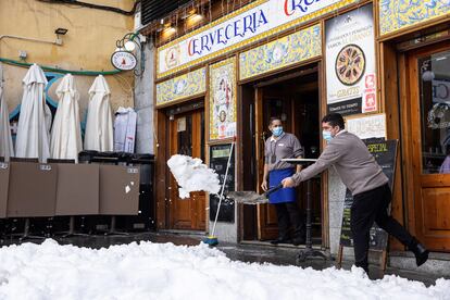 Trabajadores de un bar limpian de nieve la terraza de un local en Madrid, este domingo.