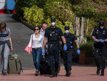 Agentes de policía con mascarillas acompañan ayer a turistas que abandonan el hotel en cuarentena en Tenerife por el coronavirus.