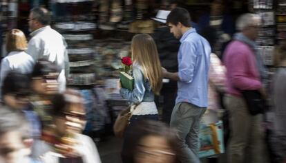 Una pareja pasea con rosa y libro, durante la jornada de Sant Jordi, por una calle de Barcelona