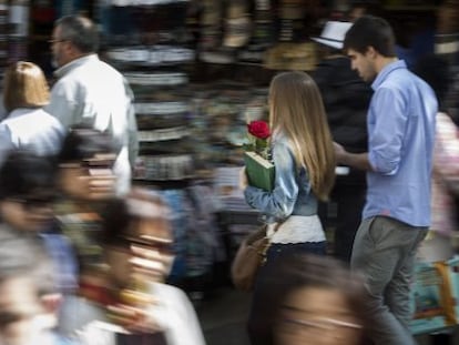 Una pareja pasea con rosa y libro, durante la jornada de Sant Jordi, por una calle de Barcelona