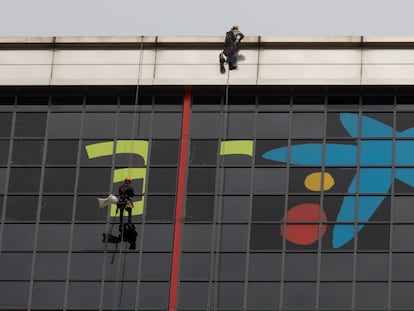 Varios operarios quitan el logotipo de Bankia para incorporar, sobre las ventanas más altas del edificio, la imagen de CaixaBank.