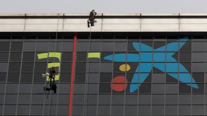 Varios operarios quitan el logotipo de Bankia para incorporar, sobre las ventanas más altas del edificio, la imagen de CaixaBank.