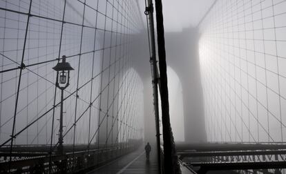 Una persona pasea por el puente de Brooklyn cubierto por una densa niebla. 