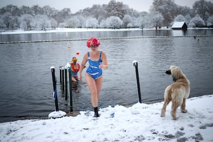 Dos bañistas salen del lago Serpentine ante la atenta mirada de un perro. 