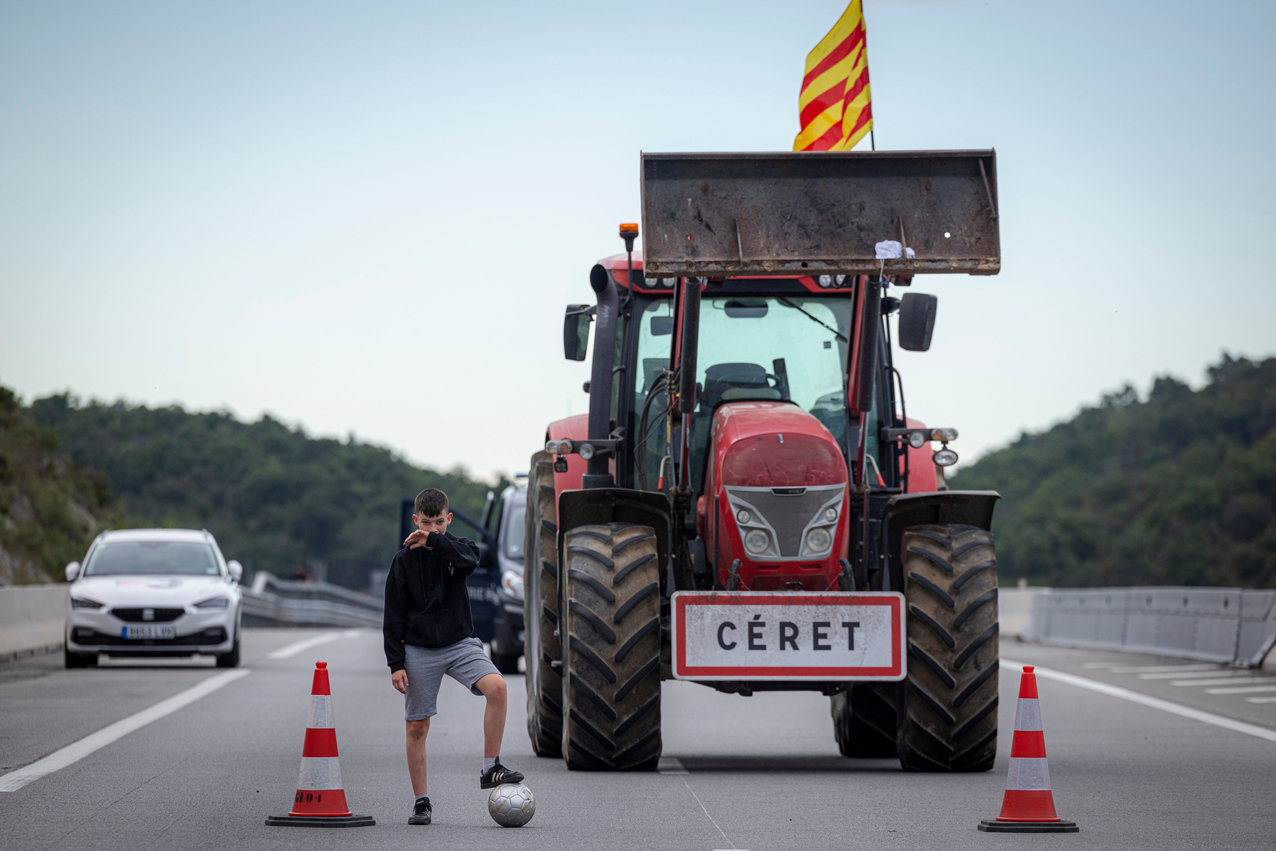 Un niño  juega con un balón junto a un tractor, en el Km 0 de la AP-7 durante la protesta agrícola.