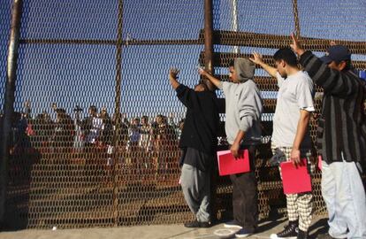 Deported migrants stand near a border fence in Tijuana, Mexico. 