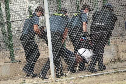 Agentes de la Guardia Civil arrastran a uno de los inmigrantes en el interior de la valla. Junto a la verja hay un fuerte despliegue policial, tanto en el lado espa&ntilde;ol como en el marroqu&iacute;.