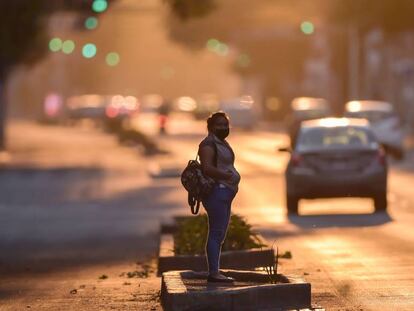 Una mujer con una mascarilla espera sobre una avenida de Ciudad de México. 
 
 