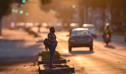 Una mujer con una mascarilla espera sobre una avenida de Ciudad de México. 
 
 