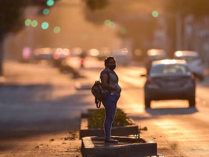 Una mujer con una mascarilla espera sobre una avenida de Ciudad de México. 
 
 