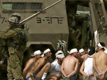 Varios presos palestinos en ropa interior esperan maniatados junto a un blindado del Ejército de Israel.