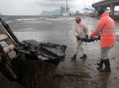 Dos trabajadores recogían ayer desechos procedentes del <i>New Flame</i> en la playa de la Concha de Algeciras.