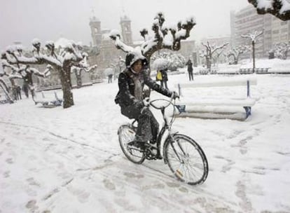 Una ciclista desafía a la nieve en los jardines de Alderdi Eder, con el Ayuntamiento donostiarra al fondo.