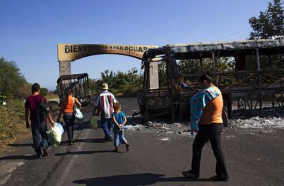 Una familia camina entre autobuses quemados después de un enfrentamiento entre cárteles locales en Michoacán.