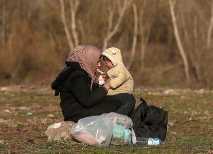 Una refugiada tranquiliza a su bebé sentada en el suelo junto a sus pertenencias, cerca de río Meric a su paso por la provincia turca de Edirne, fronteriza con Grecia, tras llegar de Siria junto a cientos de migrantes para adentrarse en territorio heleno.