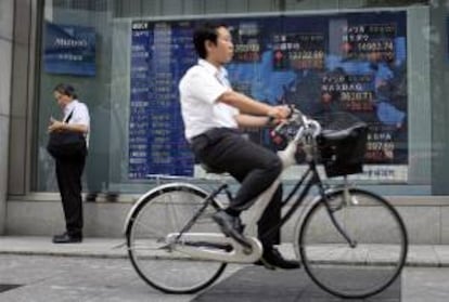 Un hombre circula en bici por delante de una pantalla con información bursátil en Tokio.