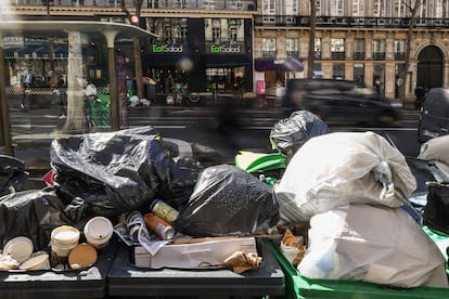 People pass by next to garbage cans overflowing with trash in Paris, France, 14 March 2023. Garbage collectors have joined the massive strikes in France against the government's pension reform plans, piling the streets of the French capital in the meantime with thousands of tonnes of garbage. 