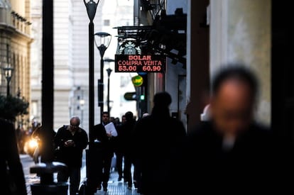 Personas caminan junto a una pizarra con el valor del dólar en Buenos Aires.