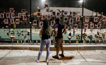 Dos personas miran un altar improvisado con los retratos de los desaparecidos en el derrumbe del edificio en Surfside. El presidente Joe Biden ha declarado este viernes el estado de emergencia en Florida, lo que permite poner a disposición de las autoridades locales recursos federales para reforzar las tareas de salvamento.