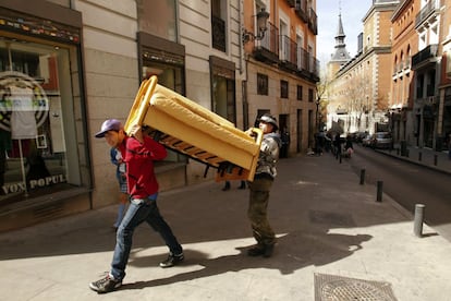 Dos vecinos se llevan un sofá a hombros justo delante del edificio desokupado.