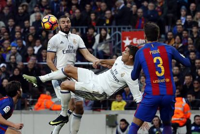 El delantero portugués del Real Madrid, Cristiano Ronaldo, intenta una chilena ante su compañero, el francés Karim Benzema (i) y el defensa del FC Barcelona Gerard Piqué (d) durante el partido de la decimocuarta jornada de Liga que disputaron frente al FC Barcelona en el Camp Nou de Barcelona, el 3 de diciembre de 2016.