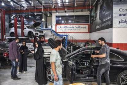 Elham, dentro de su vehículo; observa cómo Saja da instrucciones a Yasin, y pregunta al mecánico cuándo podrá pasar a recoger el coche.