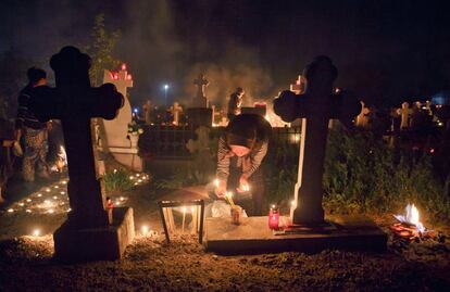 Una mujer enciende una vela junto a unas tumbas en un cementerio durante un memorial de Domingo de Ramos ortodoxo para los difuntos de Herasti, Rumania.