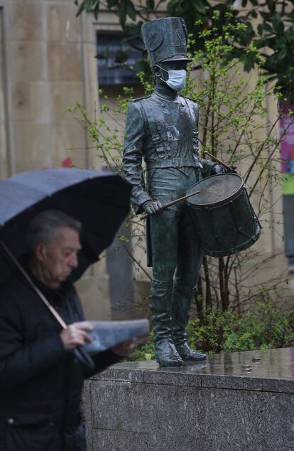 Un ciudadano pasa frente a una escultura de un tamborrero a la que le han puesto una mascarilla sanitaria, este lunes en San Sebastián.