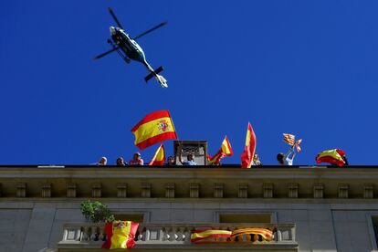 Helicóptero sobrevoa um edifício de Barcelona enquanto um grupo de manifestantes agitam bandeiras espanholas.