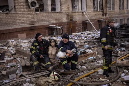 Dos bomberos posan el lunes con un maniquí dañado encontrado entre los escombros después de que un centro comercial y los edificios circundantes fueran alcanzados por un ataque con misiles rusos en Járkov, en el noreste de Ucrania.
