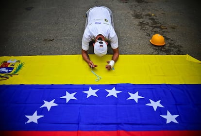 Un opositor reza sobre una bandera nacional durante una marcha contra Maduro el 1 de mayo de 2017 en Caracas.