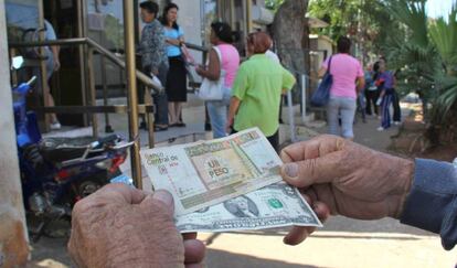 Un hombre muestra un peso convertible cubano y un dólar estadounidense frente a una oficina de la Western Union en La Habana (Cuba).