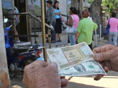 Un hombre muestra un peso convertible cubano y un dólar estadounidense frente a una oficina de la Western Union en La Habana (Cuba). 