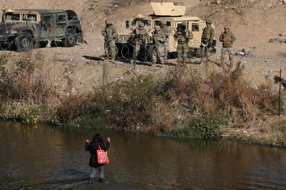 Una migrante cruza el Río Bravo con las manos en alto, frente a la valla de púas colocada por agentes de la Guardia Nacional de Texas.