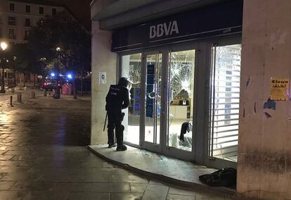 Un policia mira el interior de una sucursal del banco BBVA a través de los cristales rotos en Lavapiés.