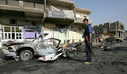 Un policía iraquí, junto a los restos del coches bomba que ha matado a cinco trabajadores.
