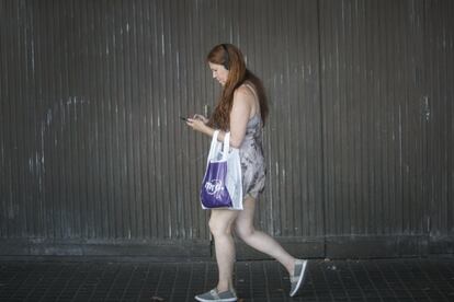 Una mujer anda mirando el móvil con los auriculares puestos.