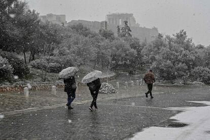 Varias personas caminan frente a la Acrópolis durante una nevada sobre la ciudad de Atenas (Grecia).