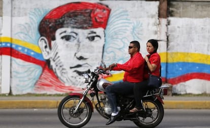 A couple rides past a street mural of Hugo Ch&aacute;vez in the city of Barinas.