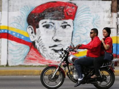 A couple rides past a street mural of Hugo Ch&aacute;vez in the city of Barinas.